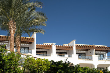 Fototapeta premium Palm trees against white home by the beach with blue sky and sand The top of the house or apartment with nice window
