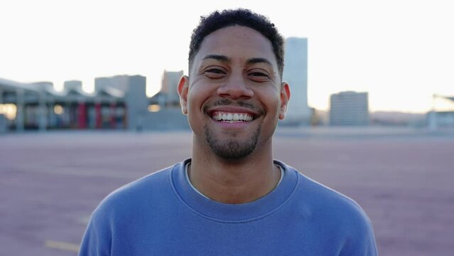 Young hispanic latino man smiling outdoors. Happy closeup face portrait of millennial teenage boy posing at camera in city street.