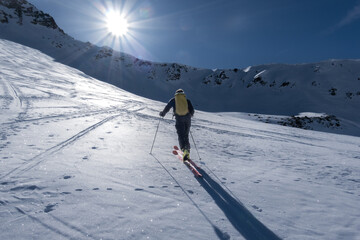 Fototapeta na wymiar Single backlit ski tourer ascending mountainside in Alps