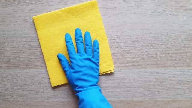 Cleaning process in kitchen. Deep Clean Kitchen in One Day concept. Hand in blue rubber glove with yellow dishrag wipes wooden table in one motion. Removal of dust and dirt.
