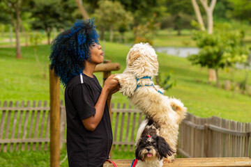 Uma jovem negra de cabelos tingidos de azul, segurando as patas dianteiras de seu cachorro que...