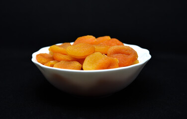 Juicy dried apricots in a white ceramic bowl. Dried apricot fruit halves without a stone.