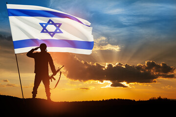 Silhouette of soldier saluting with Israel flag against the sunrise in the desert.