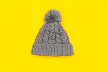 Knitted grey winter hat with pompon on bright yellow background. Cozy knitted accessory in trendy color, warm concept. Flat lay, copy space.