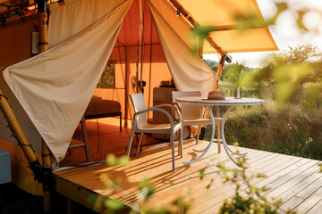Cozy open glamping tent with light inside during sunset. Luxury camping tent for outdoor summer...