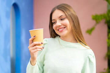 Young pretty blonde woman holding a take away coffee at outdoors with happy expression