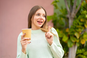 Young pretty blonde woman holding a take away coffee at outdoors intending to realizes the solution while lifting a finger up