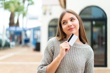 Fototapeta premium Young pretty blonde woman holding a credit card and thinking
