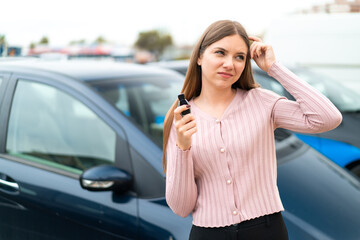 Young pretty blonde woman holding car keys at outdoors having doubts and with confuse face...