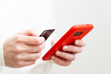 Close up of female hands holding credit card and using smartphone in red case on white background. Woman paying securely online, using banking service, ordering in internet store. Online shopping