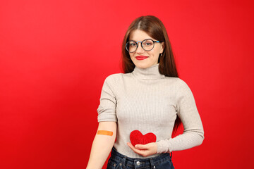Smiling woman after donating blood with a band-aid on her hand holds a red heart in her hands.