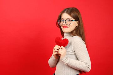 A young woman volunteer donates blood, holds a heart in her hands on a red background.