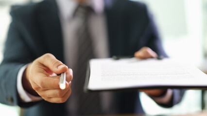 Manager holding out paper document on clipboard and pen for signing closeup