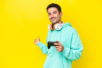 Young handsome man playing with a video game controller over isolated wall extending hands to the...
