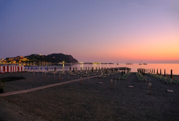 Obraz premium sunset on the beach with yellow sunbeds over the sea and horizon and hills with hotels. Sestri Levante, Liguria, Italy 