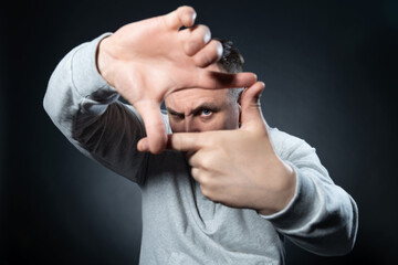 Fototapeta premium Portrait of a man in a white sweatshirt making a crop with his fingers while looking at the camera, on a black background