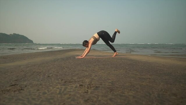 Stretching woman yoga on beach doing sun salutation asana flow, healthy brunette workout