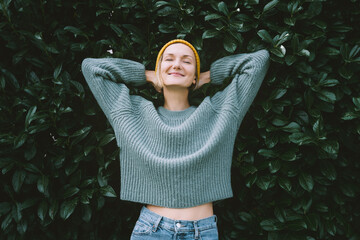 Portrait of relaxed and confident woman with eyes closed on background of green leaves wall. Thoughtful person in front of green hedge. Joy, zen and balance people. Stability through mental health - 584717970