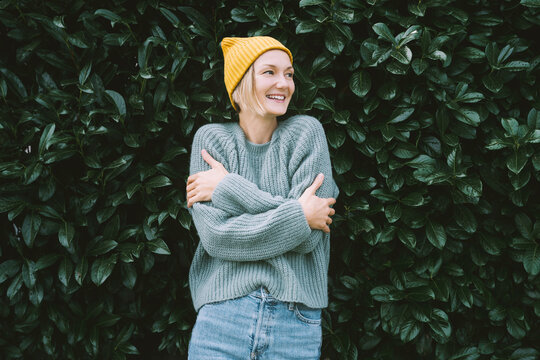 Photo of friendly smiling attractive woman on background of green hedge. Happy confident woman in front of green leaves wall. Thoughtful person outdoors at autumn season.