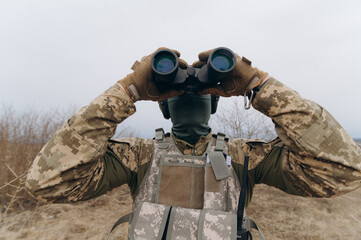 a soldier in camouflage holds binoculars. military man holding binoculars