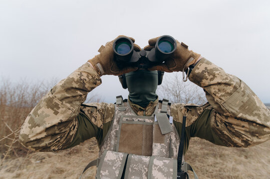 a soldier in camouflage holds binoculars. military man holding binoculars