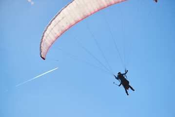 Skydiver on blue paraglider in blue sky. and a white trail from the plane in the sky