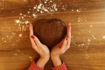 Close-up image of dough kneaded in heart shape and framed by hands. A visual evoking the love of making pastries, cakes and cookies and cooking for your loved ones.