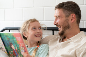 Fototapeta premium Little girl's father read stories to children before going to bed to unwind and sleep soundly until the morning.