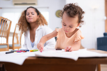 A little child's imagination is represented through colored pencil drawings, with the mother attentively supervising in the living room of the house.