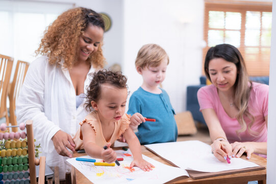 A little child's imagination is represented through colored pencil drawings, with the mother attentively supervising in the living room of the house.