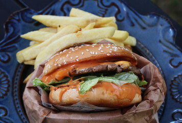Hamburger with cheese and fried potatoes on a blue plate