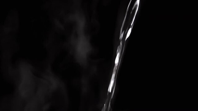 Jet of Hot Boiling Water a Pouring on the Background of Clouds White Steam. Evaporation of steam on a black background. A falling transparent jet of hot water. Splash, drops. Vapor cloud. Blurred fog.