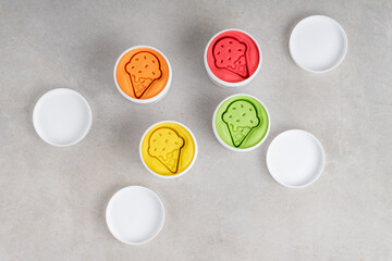 Colorful dough in white jars on gray background. Flat lay