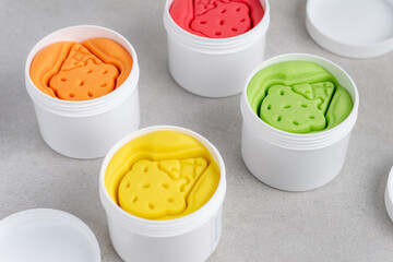 Colorful dough for kids play in white plastic jars.