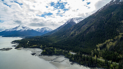 Naklejka premium Aerial view of a snowy mountain range covered with clouds against a lake in Hope, Alaska