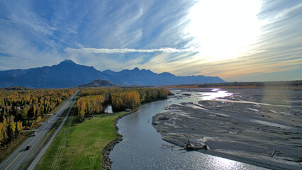Aerial view of the Matanuska River surrounded by autumn trees against mountains in Palmer, Alaska - obrazy, fototapety, plakaty