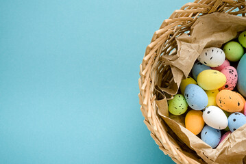 Eggs painted blue, yellow, green and pink on a blue background in a basket on a blue background. Copy space for text.