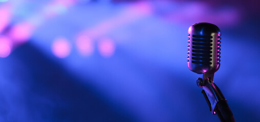 Vintage vocal microphone in the dark on a concert stage with pink and blue spot lighting. Live music or podcast wide banner background with copy space - obrazy, fototapety, plakaty