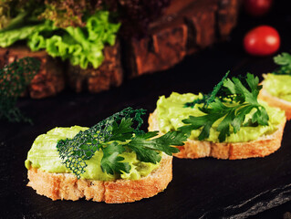 Toasts with avocado guacamole on black wood