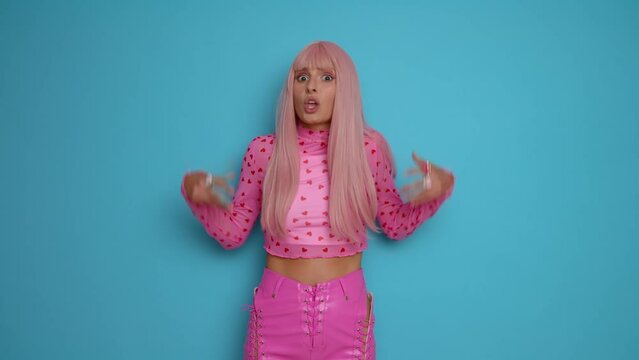 Young model woman with long pink hair and in pink clothes standing in the midle of blue background, shakes her head, shrugs shoulders showing disappointment, copy space high quality video.