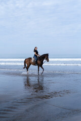 Young woman riding a horse on the beach at the ocean.