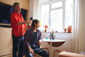 Same Sex Male Couple At Home With Man Styling Partner's Hair