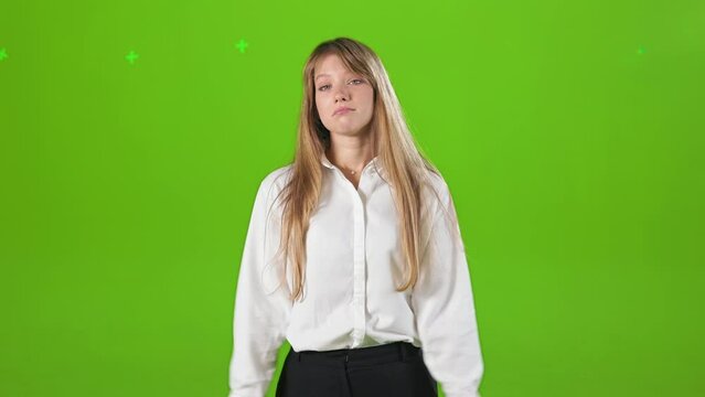 Front view of young, blonde female standing baffled in studio. Beautiful female wearing official clothes, stretching hands, asking. Isolated on green studio background.
