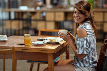 Young woman with beautiful smile holding coffee cup and feeling joyful.