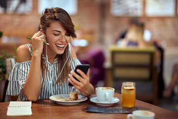 Cheerful young woman on a video call with friend while she is in cafe alone.