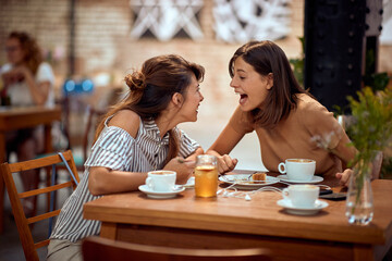 Girlfriends having a very cheerful conversation in cafe. Laughing, giggling.
