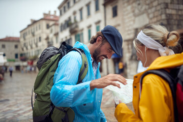 Navigating through new city, couple in raincoats on walk. Joyful man and woman on holiday. Travel, togetherness, city, lifestyle concept.