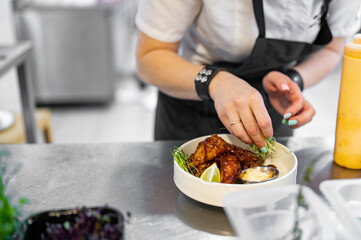 woman chef cooking chicken wings in a sauce in the kitchen