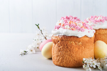 Obraz na płótnie Canvas Traditional Easter sweet bread or cakes with white icing and sugar decor, colored eggs and cherry blossom tree branch over white table. Various Spring Easter cakes. Happy Easter day. Selective focus.