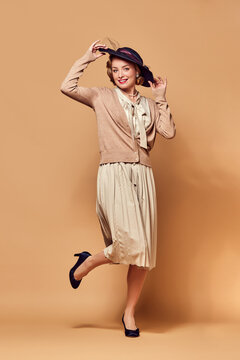 Portrait of charming lady wearing hat smiling at camera over beige background. Music, dance, charm, grace concept